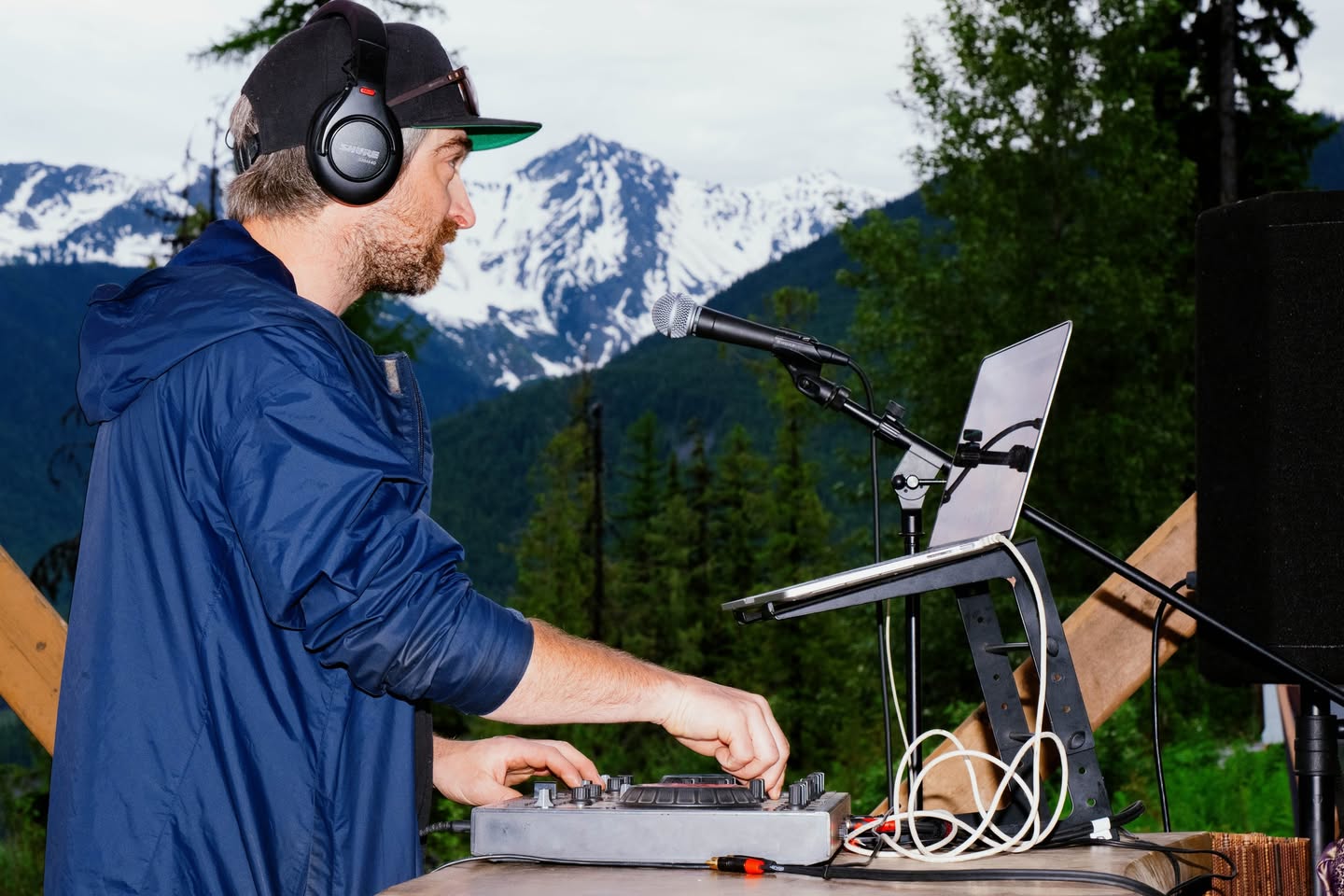 DJ performing outdoors with mountains in the background